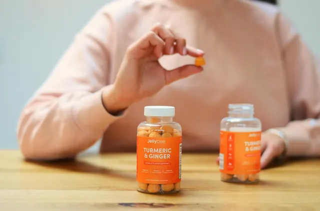 Усмихната жена държи бутилка с витамини в светла, уютна обстановка, олицетворяваща здравословен начин на живот